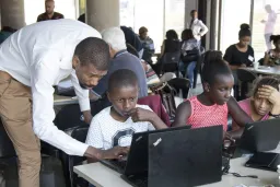 Male teacher assisting seated student at computer