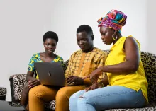 Three university-age people - one man with a woman on either side - sitting on a couch using a laptop